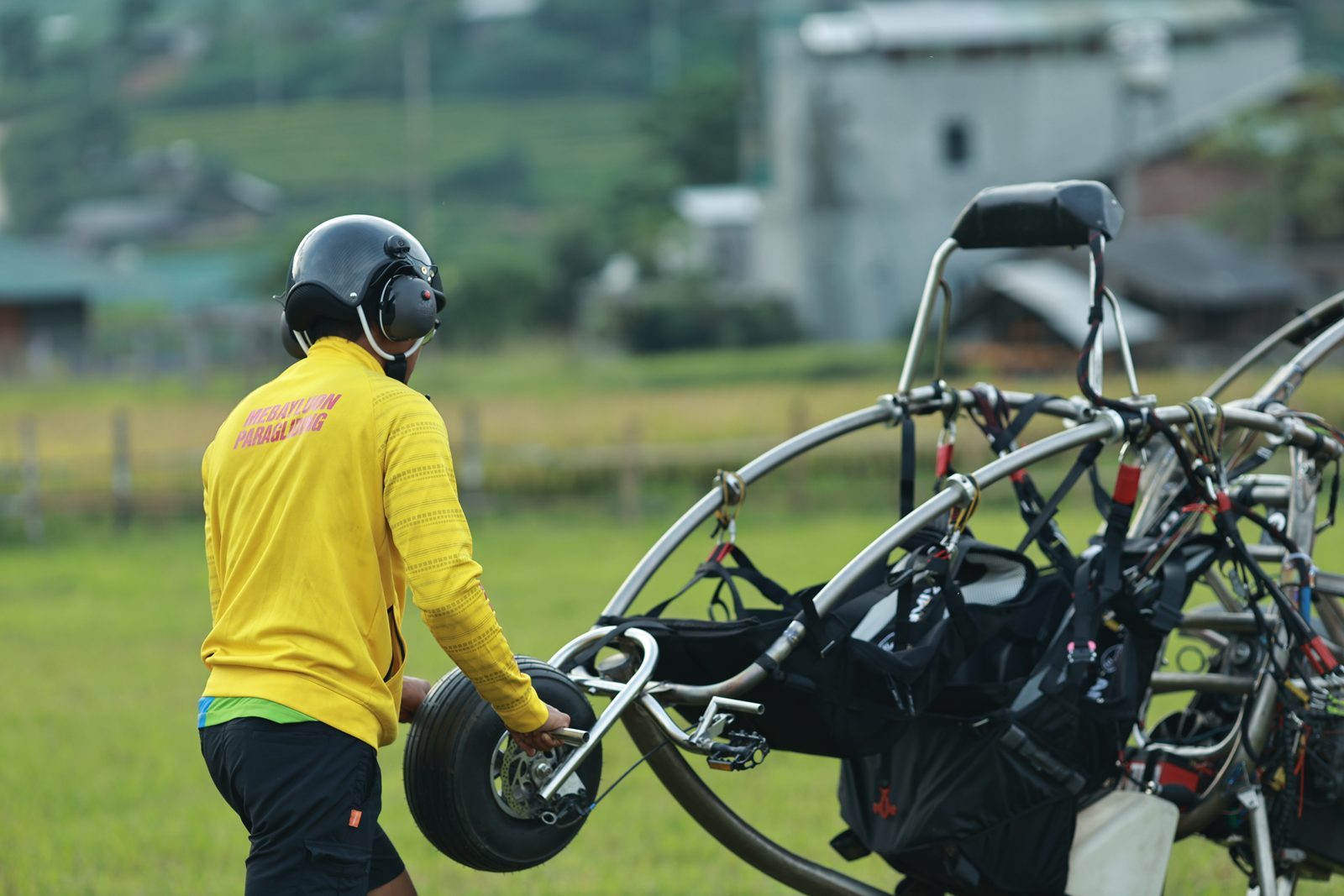 Ein Tandem-Paramotor zieht auf einer ebenen Wiese den Schirm auf, der Passagier vorne, der Pilot dahinter, kurz vor dem Startlauf