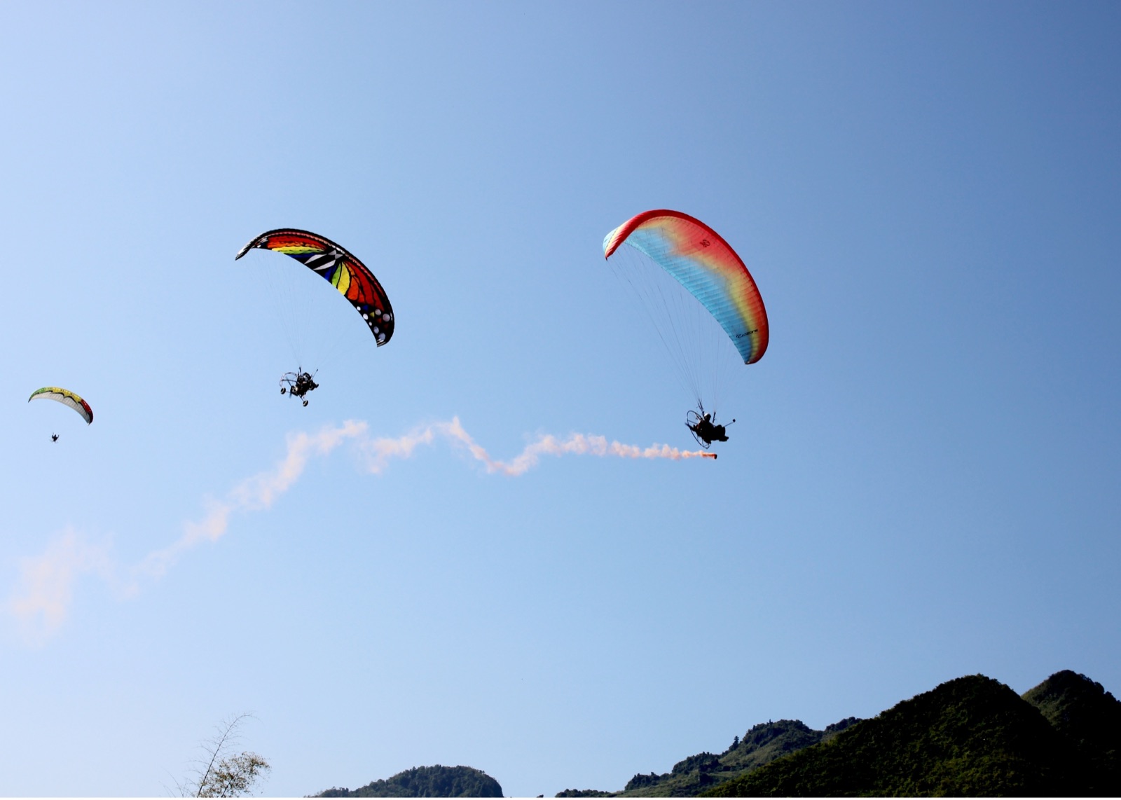 Ba cánh dù paramotor kéo khói màu trên núi đá Hà Giang